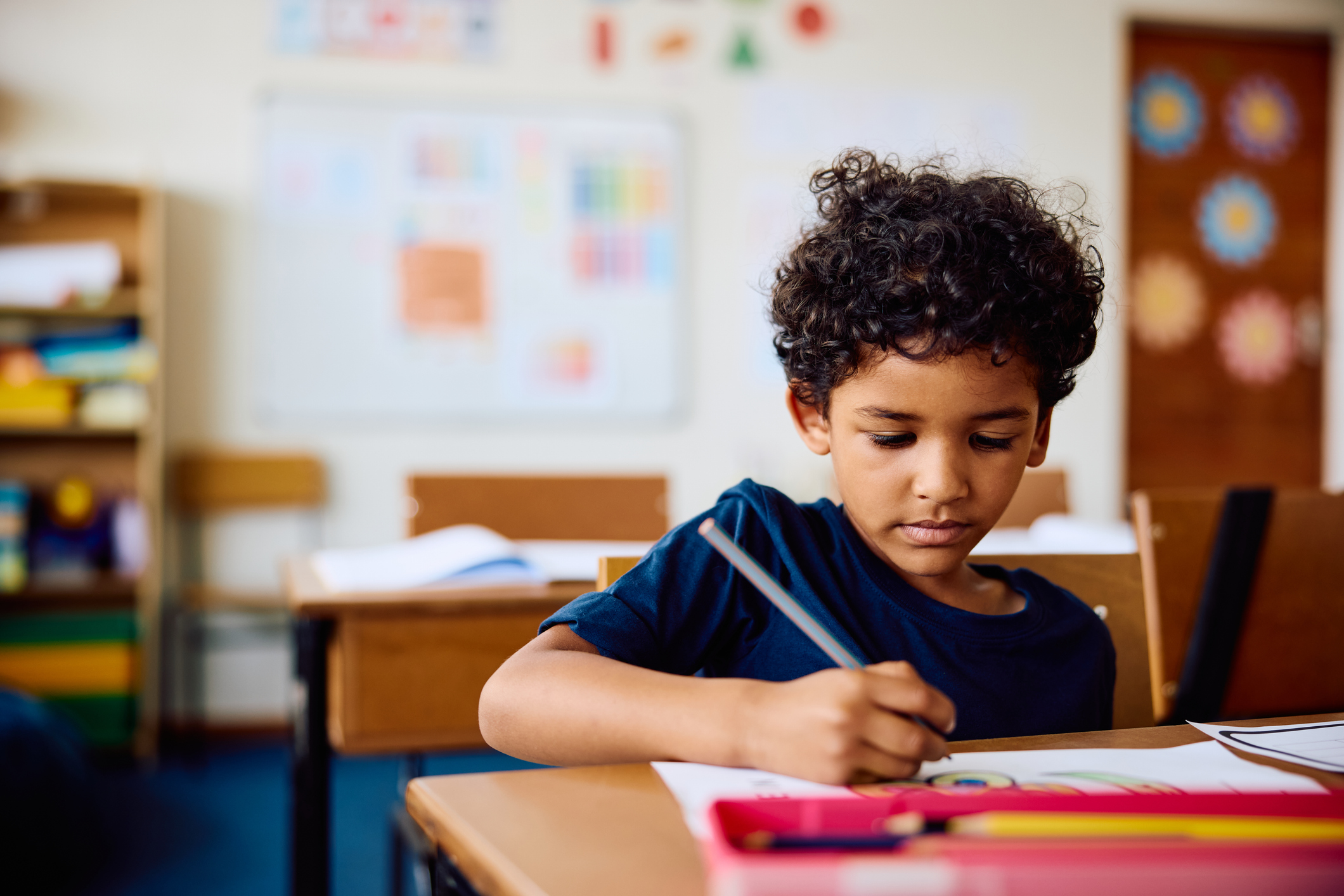Elementary schoolboy working in class, writing in notebook, concentrating
